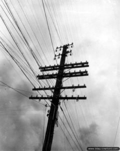 Des civils français sont réquisitionnés pour réparer les lignes électriques dans Carentan. Photo : US National Archives