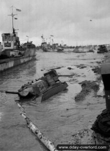 Un char Sherman, piégé par un trou d'eau sur la plage de Gold, a été abandonné. Des navires LCT sont visibles à proximité. Photo : IWM