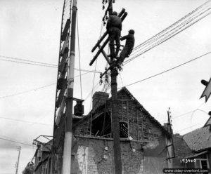 Des civils français sont réquisitionnés pour réparer les lignes électriques dans Carentan. Photo : US National Archives