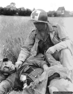 Le caporal Roy C. Moore inspecte la blessure d’un blessé allemand allongé dans un champ du secteur de Saint-Lô. Photo : US National Archives