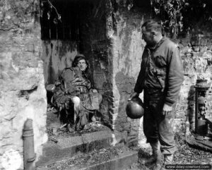 27 juin 1944 : le capitaine Earl J. Topley face au cadavre d’un soldat allemand sur des marches devant un portail de la rue Armand Levéel à Cherbourg. Photo : US National Archives