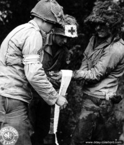 Deux infirmiers appliquent un bandage à un soldat américain blessé au poignet et qui a maculé son pantalon de sang (photo prise pendant les combats du 10 au 13 juillet 1944) dans le secteur de Saint-Lô. Photo : US National Archives