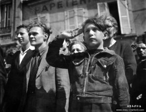 27 juin 1944 : cérémonie de la libération devant de l’hôtel de ville de Cherbourg, durant laquelle un enfant effectue un salut militaire. Photo : US National Archives