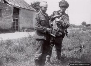 Le soldat Durston, de la A Coy, 9th Battalion avec un prisonnier allemand blessé près du carrefour de l'Ecarde et du château d'Amfreville (la tête de mort est un signe de reconnaissance anglais pour l'attaque en planeur de la batterie de Merville). Photo : IWM