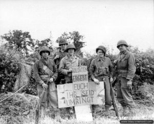 Des soldats du 83rd Armored Reconnaissance Battalion de la 3rd (US) Armored Division posent dans le secteur de Saint-Lô à côté d’une pancarte en carton où il est écrit en allemand : « soldats, rendez-vous, vous êtes encerclés ». Photo : US National Archives