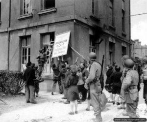 28 juin 1944 : des civils et des soldats américains ôtent le panneau indiquant le siège principal de l’organisation Todt, rue Dom-Pedro à Cherbourg. Photo : US National Archives