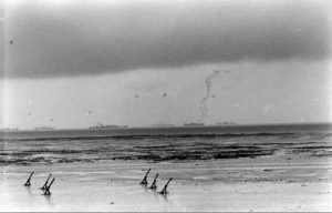 Au large de Grandcamp-les-Bains, des navires de guerre alliés croisent en large. Sur la plage, des défenses de plage baptisées "Holzfähle" et surmontées de mines antichar "Tellermine". Photo : US National Archives