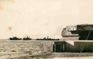 Après-guerre, la casemate Vf600 d'Asnelles, qui abritait un canon de 50 mm, avec les vestiges des navires brise-lames du Mulberry B.