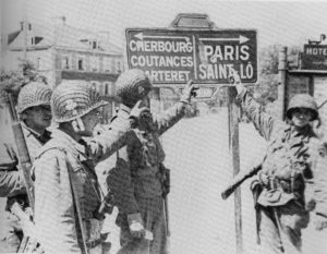 Des soldats aérotransportés du 327th Glider Infantry Regiment, 101st (US) Infantry Division, devant un panneau Place Vauban à Carentan. Photo : US National Archives