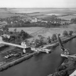 Carte postale d'après-guerre de Bénouville, prise en direction du nord-nord-ouest et de son fameux pont à bascule devenu le "Pegasus Bridge". En haut à droite de la photo, les maisons d'Ouistreham-Riva-Bella sont visibles. Photo : DR