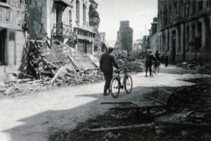 Des civils circulent dans les décombres de la rue de Caen à Lisieux après les bombardements de juin 1944. Photo : DR