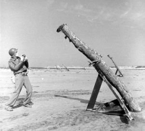 Devant le point d'appui Wn 81, sur la plage de Grandcamp-les-Bains, un photographe américain devant des obstacles de plage baptisés "Holzfähle" et surmontés de mines antichar "Tellermine". Photo : US National Archives