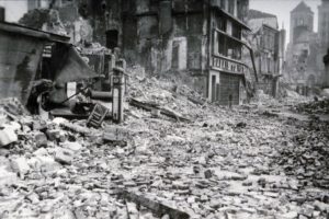 Les ruines de la rue Henry Chéron à Lisieux après les bombardements de juin 1944. Les vestiges du garage Jonquart (et sa pompe à essence) et du magasin "Palais du Vêtement" sont visibles. Photo : DR