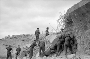 Des sapeurs anglais du Royal Engineer ouvrent une brèche à travers le mur antichar à Arromanches pour accueillir les prochains axes logistiques du port artificiel Mulberry B. Photo IWM A 24170