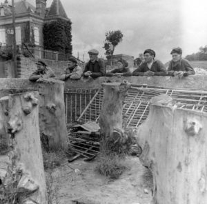 Des civils accoudés au mur antichar interdisant l'accès au port de Grandcamp-Les-Bains, à l'intersection de l'actuelle rue Aristide Briand et du quai Chéron. Photo : US National Archives