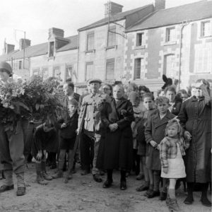 4 juillet 1944 : à l'occasion de la fête nationale américaine, la population de Cerisy-la-Forêt assiste à la cérémonie organisée devant le monument aux Morts sur la place du marché. Parmi les habitants, un vétéran décoré de la Première Guerre mondiale. Photo : US National Archives