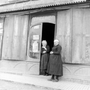 En centre-ville de Cerisy-la-Forêt, place du marché, deux habitantes se tiennent à l'entrée de l'épicerie. Photo : US National Archives