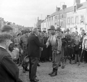 4 juillet 1944 : à l'occasion de la fête nationale américaine, le maire de Cerisy-la-Forêt, Eugène Godin, et le Major General Walter M. Robertson, commandant la 2nd (US) Infantry Divison, se serrent la main au début de la cérémonie organisée devant le monument aux Morts. Photo : US National Archives