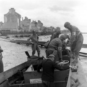 Des sapeurs et des infirmiers américains, accompagnés de civils, observent un chaland de débarquement LCVP échoué sur le débarcadère de Grandcamp (quai Crampon) peu après la libération en 1944. Ce LCVP était rattaché à l'USS Joseph T. Dickman déployé au large d'Utah Beach le 6 juin 1944. Photo : US National Archives