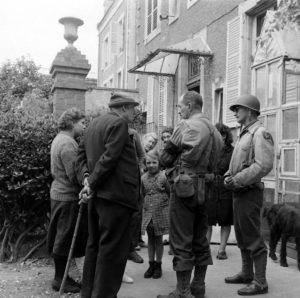 Le sergent Roland des Autels (sans son casque) du CIC (Counter Intelligence Corps) s'entretient avec des habitants de la commune de Grandcamp-les-Bains. Avec la canne, Pierre Ferrari, conseiller municipal de Grandcamp-les-Bains. Photo : US National Archives