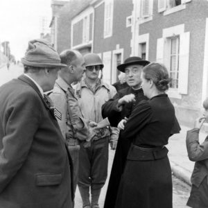 Le sergent Roland des Autels (sans son casque) du CIC (Counter Intelligence Corps) s'entretient avec des habitants de la commune de Grandcamp-les-Bains, sur l'actuelle rue de la libération. A gauche, Pierre Ferrari, conseiller municipal de Grandcamp-les-Bains. Photo : US National Archives