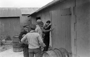 Un sergent américain accompagne des civils à Grandcamp-les-Bains pour inspecter une remise, devant laquelle des fûts de carburant ont été déposés. Photo : US National Archives