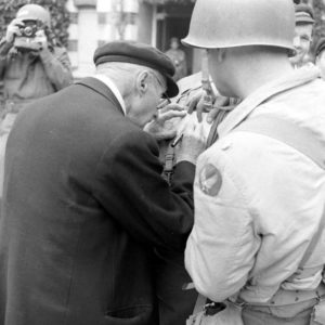 Rue Gambetta à Grandcamp-les-Bains, un civil rédige des informations pour les Américains. Le badge visible au premier plan est celui de l'Army Air Force. Photo : US National Archives