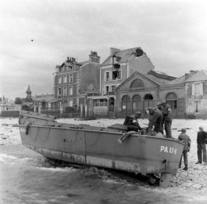 Des sapeurs et des infirmiers américains, accompagnés de civils, observent un chaland de débarquement LCVP échoué sur le débarcadère de Grandcamp (quai Crampon) peu après la libération en 1944. Ce LCVP était rattaché à l'USS Joseph T. Dickman déployé au large d'Utah Beach le 6 juin 1944. Photo : US National Archives