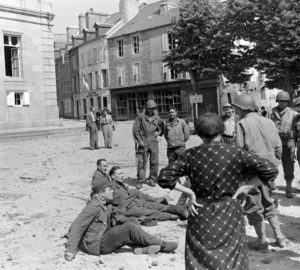 Sur la place Littré d'Avranches, couverte de débris, des prisonniers allemands attirent la curiosité de la population, sous contrôle des militaires américains. Photo : US National Archives