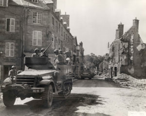 Rue de la Constitution à Avranches, un convoi de half-tracks et de camions appartenant au 68th Tank Battalion, 6th (US) Armored Division, progresse dans la ville. Photo : US National Archives