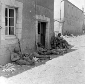 Épuisés par les éprouvants combats qu'ils viennent de livrer, des soldats aérotransportés américains de la 101st (US) Airborne Division se reposent le long de la rue Holgate à Carentan. Photo : US National Archives