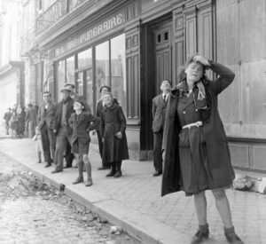 Place de la République à Carentan, alors que des avions survolent la ville, des civils observent les mouvements américains. Photo : US National Archives