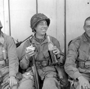 Trois parachutistes américains de la 101st (US) Airborne savourent un moment de détente après les combats de la libération de Carentan, profitant du vin et du camembert, qui améliorent la ration quotidienne et le pain de guerre. Photo : US National Archives
