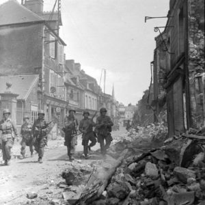 Rue Holgate à Carentan, des parachutistes de la 101st (US) Airborne Division patrouillent au milieu des décombres. Photo : US National Archives