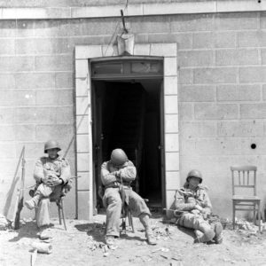 Épuisés par les éprouvants combats qu'ils viennent de livrer, des parachutistes américains de la 101st (US) Airborne Division profitent d'une sieste au soleil, en face du restaurant Désiré Ingouf à Carentan. Photo : US National Archives