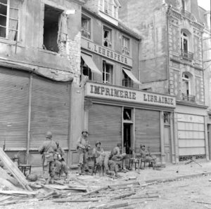 Des soldats aérotransportés américains de la 101st (US) Airborne Division devant la librairie L. Leherpeur, rue du Docteur Caillard à Carentan. Photo : US National Archives