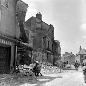 Des parachutistes américains de la 101 (US) Airborne Division dans la rue Holgate à Carentan, au pied des bâtiments détruits par les bombardements. Photo : US National Archives