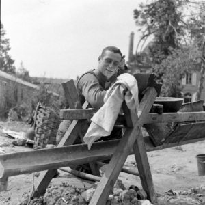 Un soldat américain en pleine toilette dans le parc de l'infirmerie tenue par le 308th Medical Battalion, 83rd (US) Infantry Division au numéro 45 rue Holgate à Carentan, dans l'hôtel Durand de la Borderie-Énouf, se repose dans le parc de la propriété. Photo : US National Archives