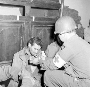 Un pensionnaire américain de l'infirmerie tenue par le 308th Medical Battalion, 83rd (US) Infantry Division au numéro 45 rue Holgate à Carentan, dans l'hôtel Durand de la Borderie-Énouf, accompagné d'un auxiliaire sanitaire. Photo : US National Archives