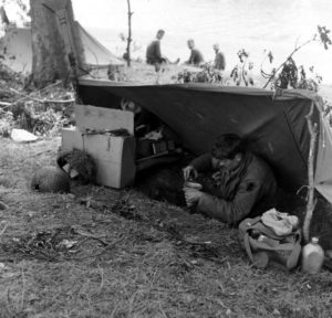 Juin 1944 : un parachutiste américain se prépare une collation à l'aide de son quart, confortablement installé dans son trou de combat réglementaire, au campement provisoire de l’état-major de la 101st (US) Airborne Division, situé au bassin à flot à Carentan. Photo : US National Archives