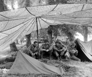 Juin 1944 : des parachutistes américains à l'abri sous des parachutes, au campement provisoire de l’état-major de la 101st (US) Airborne Division, situé au bassin à flot à Carentan. Photo : US National Archives