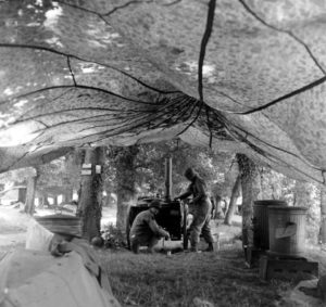 Juin 1944 : des parachutistes américains, à l'abri sous des parachutes, mettent en oeuvre une roulante allemande de prise, une Grosse Feldküche Hf.13, surnommée "Gulaschkanone" (le canon à goulache), au campement provisoire de l’état-major de la 101st (US) Airborne Division, situé au bassin à flot à Carentan. Photo : US National Archives