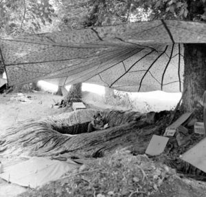 Juin 1944 : un parachutiste américain dans son trou de combat aménagé avec des parachutes, au campement provisoire de l’état-major de la 101st (US) Airborne Division, situé au bassin à flot à Carentan. Photo : US National Archives