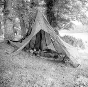 Juin 1944 : un parachutiste américain se repose dans son abri aménagé avec des parachutes, au campement provisoire de l’état-major de la 101st (US) Airborne Division, situé au bassin à flot à Carentan. Photo : US National Archives