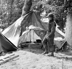 Juin 1944 : un parachutiste américain à hauteur des abris aménagés avec des parachutes, au campement provisoire de l’état-major de la 101st (US) Airborne Division, situé au bassin à flot à Carentan. Photo : US National Archives