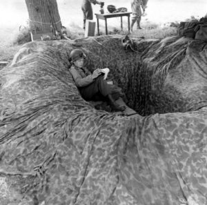 Juin 1944 : un parachutiste américain dans son trou de combat aménagé avec un parachute, au campement provisoire de l’état-major de la 101st (US) Airborne Division, situé au bassin à flot à Carentan. Photo : US National Archives
