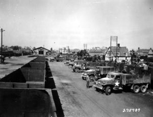 15 août 1944 : en gare de Carentan, des camions GMC sont chargés de transporter des munitions Transport de munitions au profit de la 625th Ordnance Ammunition Company. Photo : US National Archives