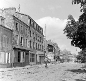 Un soldat américain progresse le long des décombres de la rue du Docteur Caillard à Carentan. Photo : US National Archives