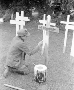 12 juillet 1944 : un prisonnier allemand peint des croix en bois (en l’occurrence celle du Gefreiter Wolfgang Müller) au cimetière militaire d'Orglandes. Photo : US National Archives