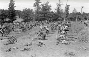 12 juillet 1944 : des prisonniers allemands creusent des tombes pour leurs camarades tués durant les combats, sous le contrôle de soldats américains au cimetière militaire d'Orglandes. Photo : US National Archives